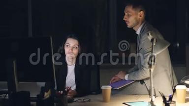 严肃的商人穿西装的男人和女人深夜在黑暗的办公室里工作，看着电脑屏幕和电脑屏幕